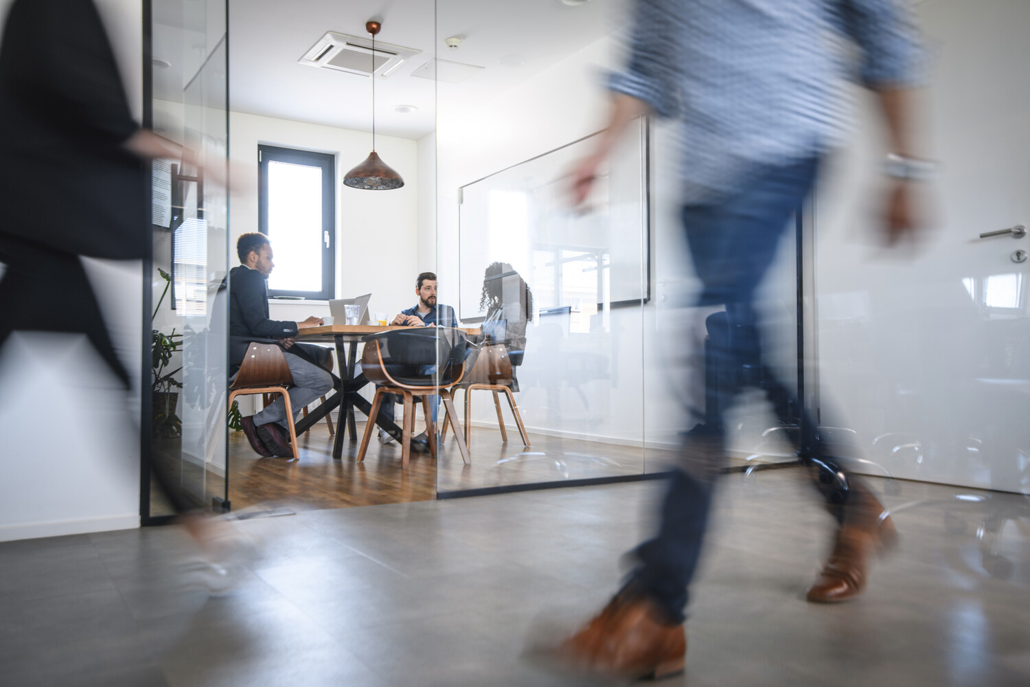 © iStock Man walking in an office with people attending a meeting